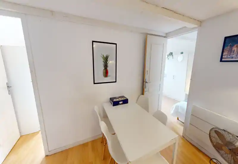 Coin repas compact et moderne avec une table blanche et quatre chaises, lumière naturelle abondante et une œuvre murale simple qui apporte une ambiance propre et confortable.