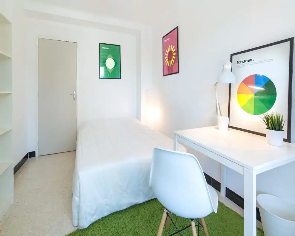 Chambre lumineuse et minimaliste avec un lit blanc bien fait, un petit bureau avec lampe, des affiches colorées et un tapis vert pour une atmosphère fraîche et calme.