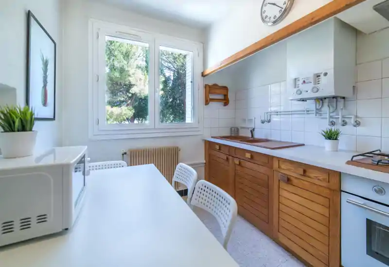 Cuisine compacte et lumineuse avec meubles en bois, évier sous une grande fenêtre et un petit coin repas — idéale pour un appartement cosy.