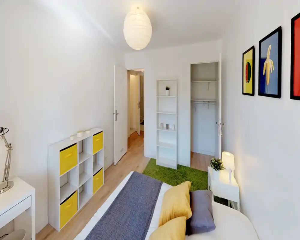 Camera da letto luminosa e ben arredata con letto comodo, cuscini soffici e una lampada sul comodino. Pareti bianche, pavimento in legno e tocchi di giallo rendono l’ambiente fresco e accogliente.