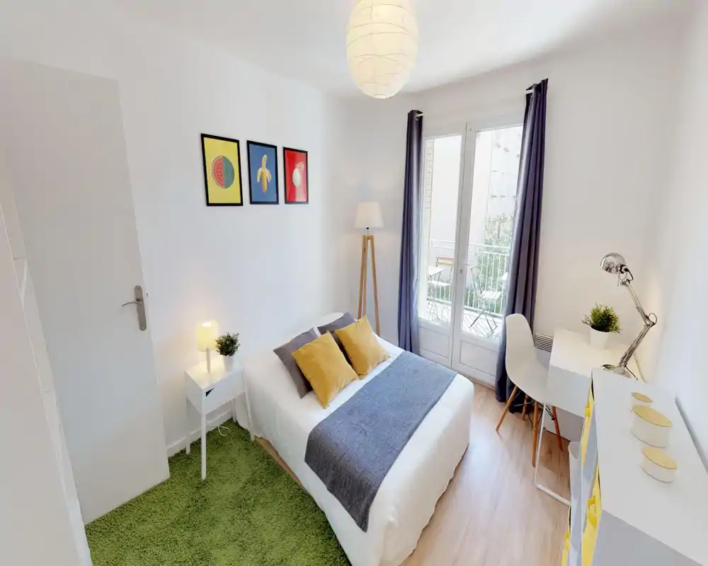 Camera da letto luminosa e ben arredata con letto matrimoniale, tessili accoglienti e una scrivania vicino alla finestra che si affaccia su un piccolo balcone. Pareti neutre, tocchi di colore e luce naturale la rendono ideale per annunci.
