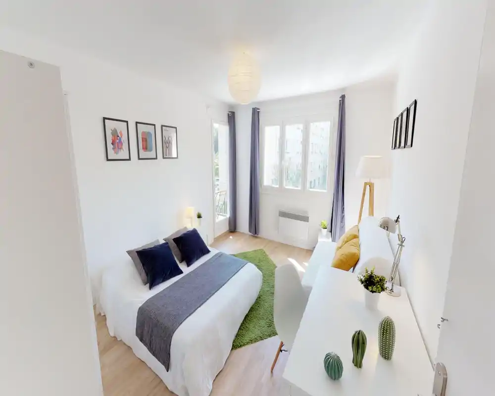Camera da letto moderna e luminosa con letto matrimoniale, cuscini decorativi, tappeto verde e un'area scrivania vicino alla finestra — ideale per affitti brevi, molto luminosa.