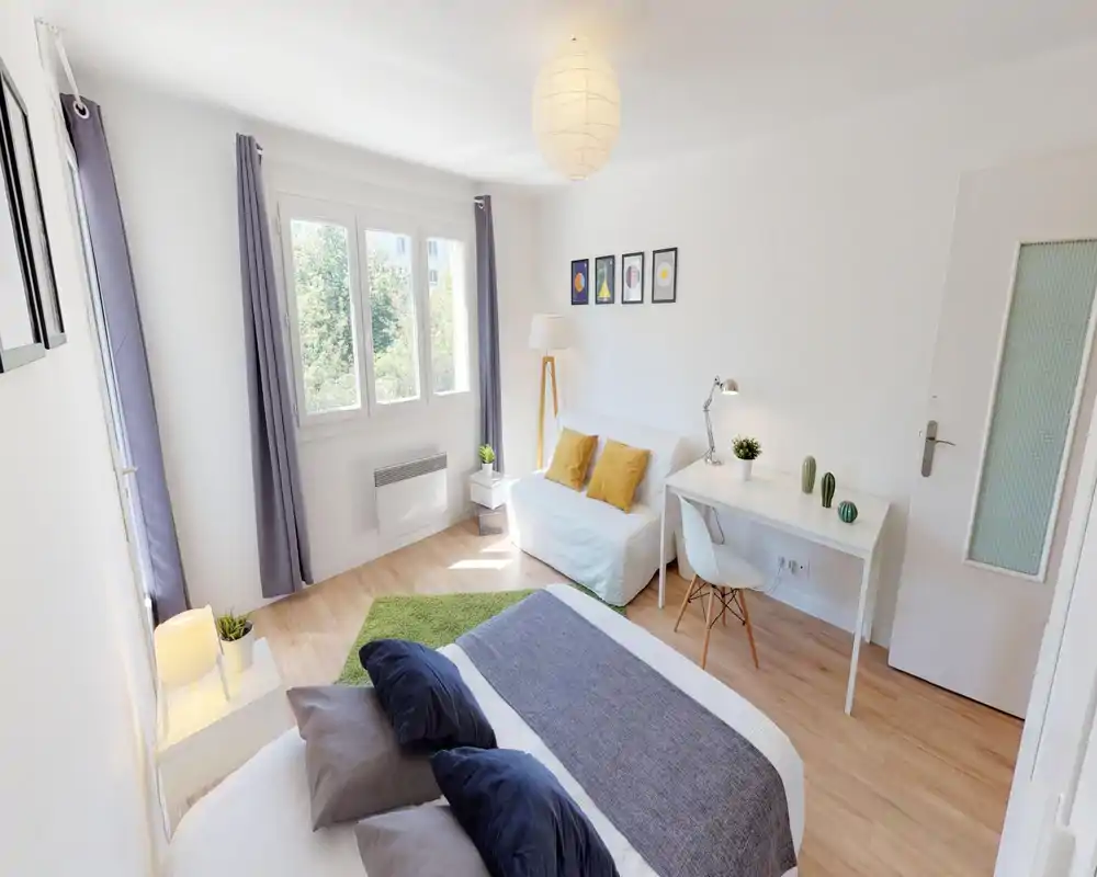 Camera da letto moderna e luminosa con ampia finestra, letto matrimoniale in primo piano, biancheria morbida e cuscini decorativi, oltre a un divanetto e una scrivania — ariosa e ben illuminata.