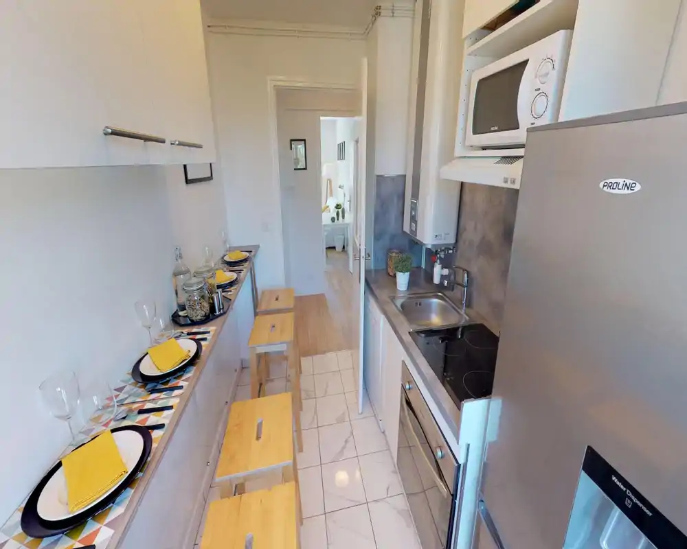 Cucina compatta e ben allestita con piano cottura, lavabo, microonde e frigorifero; un bancone stretto con sgabelli e piatti apparecchiati dona un’atmosfera accogliente e funzionale.