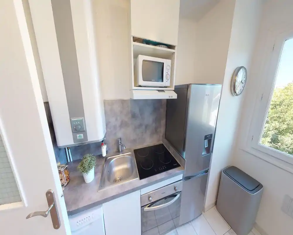 Cucina moderna e compatta con piano a induzione, forno integrato, microonde e frigorifero in acciaio. Spazio luminoso e ordinato con piccolo lavello e piano di lavoro, perfetto per un appartamento ristretto.
