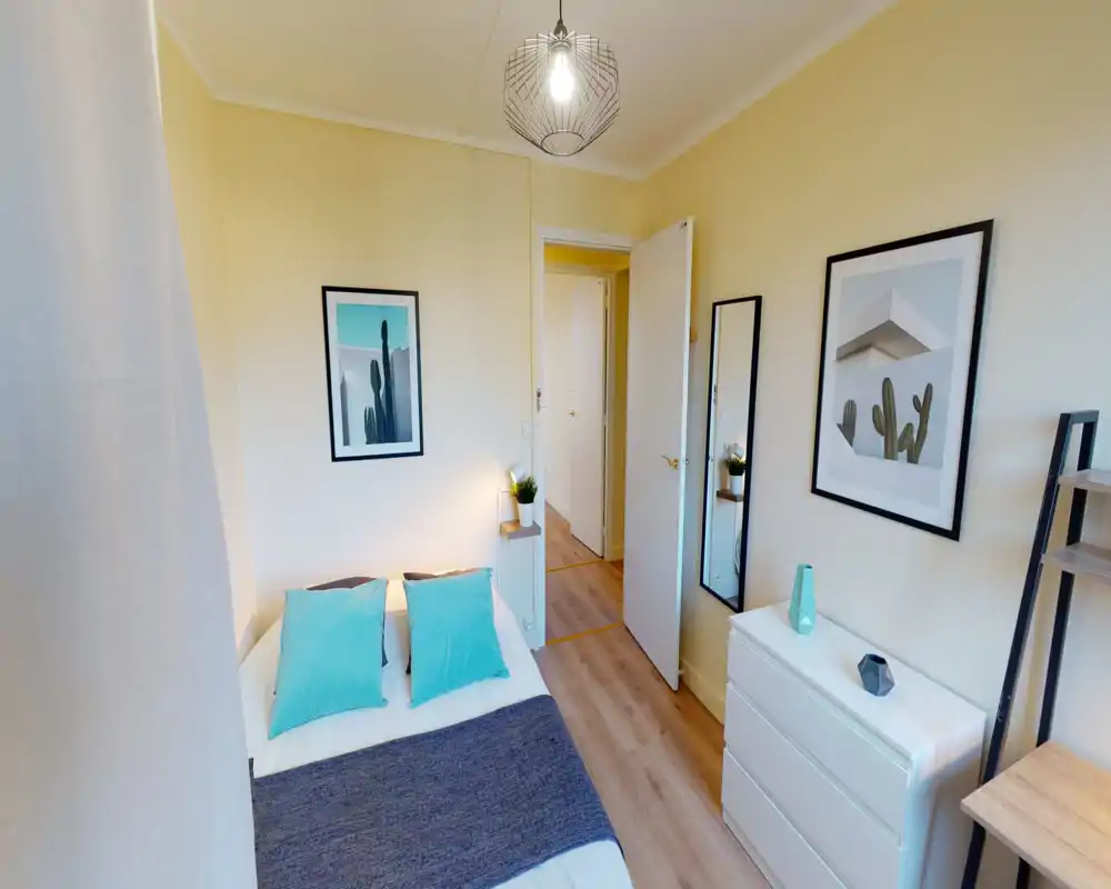Bright, modern bedroom with a neatly made double bed accented by turquoise cushions, framed wall art, a white dresser and a tall mirror — ideal for a cozy rental listing.