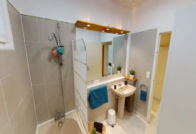 Salle de bain lumineuse et soignée avec baignoire/douche, lavabo sur pied, grand miroir et équipements modernes — idéale pour les locations de courte durée.