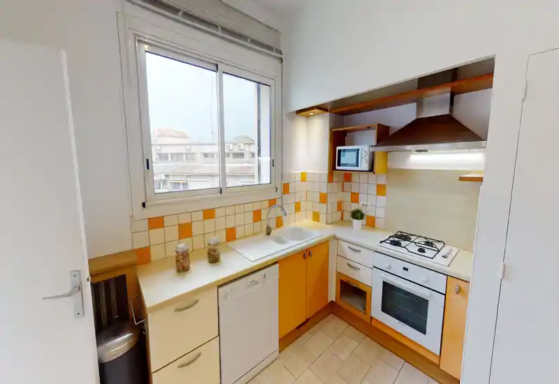 Cuisine compacte et bien équipée avec plaque à gaz, four, lave-vaisselle et fenêtre lumineuse. Carrelage orange et blanc et éclairage soigné pour un espace de cuisson agréable.