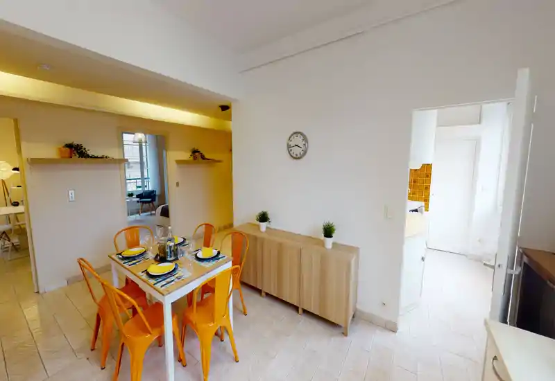 Espace repas lumineux et bien décoré avec une table pour quatre et des chaises orange chaleureuses, idéal pour des repas conviviaux.