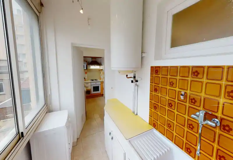 Couloir kitchenette/buanderie étroit avec grandes fenêtres, crédence orange rétro et vue sur la cuisine principale — espace lumineux et plein de caractère, adapté aux petits appartements.