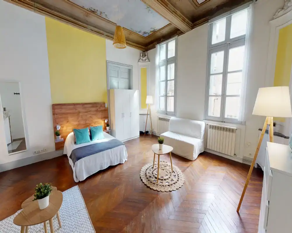 Ampia camera/studio luminosa con testata in legno, letto matrimoniale con biancheria bianca e cuscini turchesi e ampie finestre che illuminano l'ambiente. Soffitto decorato e pavimento a spina di pesce conferiscono carattere e calore.