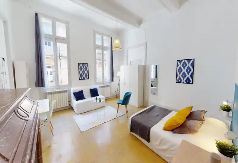 Camera da letto/studio luminosa e di design con letto matrimoniale confortevole, tessili accoglienti e grandi finestre che illuminano l’ambiente. Spazio arredato in modo funzionale con divano, sedia e armadio.