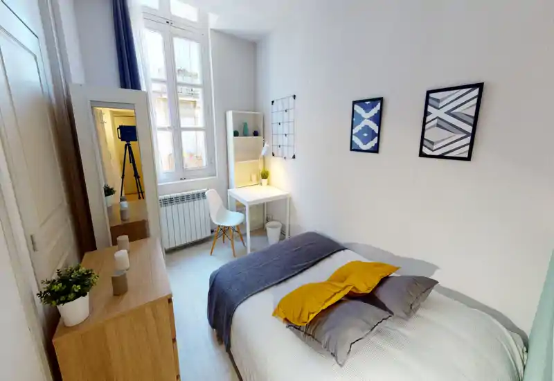 Camera da letto luminosa e ben arredata con letto matrimoniale, tessili accoglienti e una piccola scrivania vicino alla finestra — ideale per studenti o professionisti che cercano una stanza compatta e luminosa.