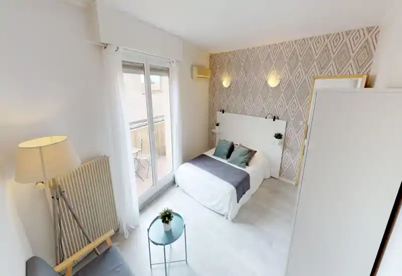Bright, stylish bedroom with a double bed, decorative cushions and patterned accent wall; large window/door opens to a small balcony letting in plenty of natural light.