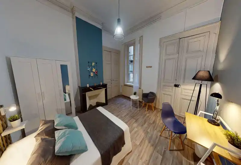 Grande chambre élégante avec lit double, armoire, bureau et coin salon; sol en bois et lumière douce pour une ambiance chaleureuse.