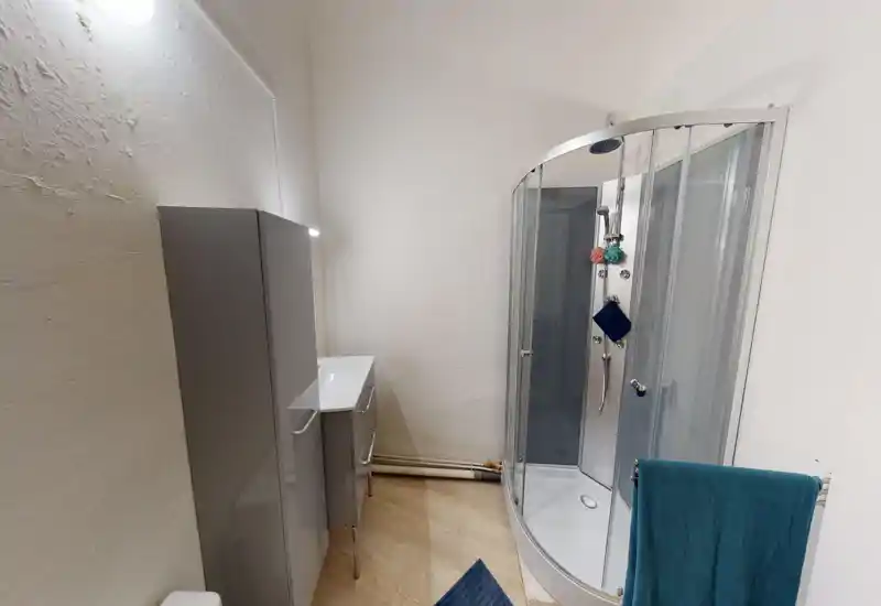 Salle de bains moderne avec cabine de douche en verre courbé, meuble vasque et porte-serviette ; agencement compact, lumineux et propre, adapté aux annonces locatives.
