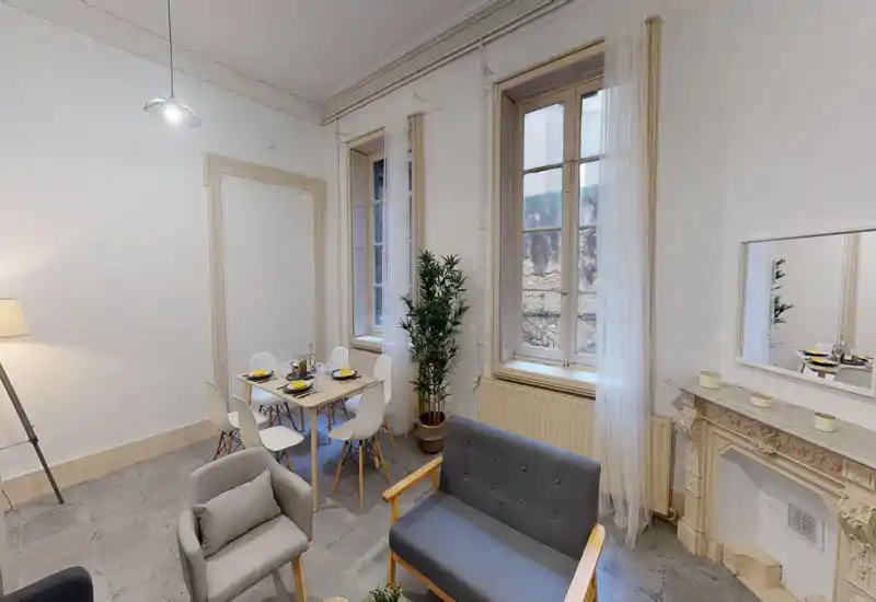 Pièce à vivre lumineuse et élégante avec une table à manger compacte, un canapé et un fauteuil confortables, une cheminée décorative et de grandes fenêtres apportant la lumière naturelle.