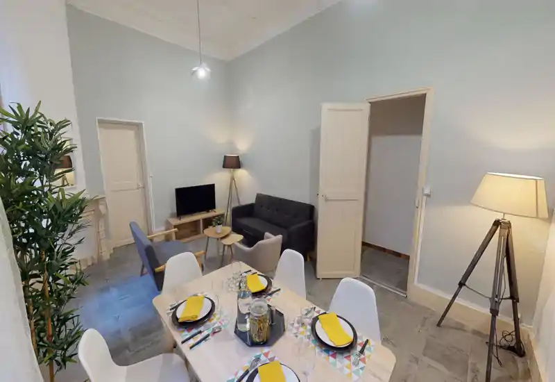 Grand séjour lumineux avec coin repas soigné, canapé, fauteuils, télévision et table dressée — idéal pour se détendre et prendre un repas.