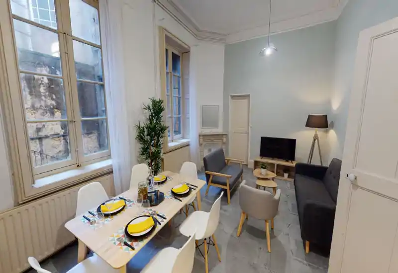 Grand espace salon/salle à manger élégant avec table dressée, sièges confortables, télévision et éclairage doux — parfait pour des séjours partagés.