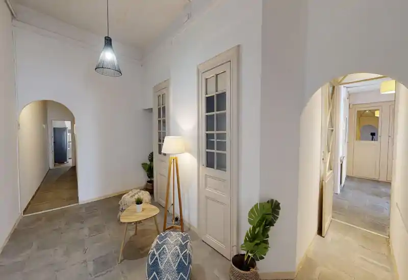 Espace salon lumineux et soigné avec murs neutres, lampe sur pied, petite table et poufs — coin chaleureux idéal pour se détendre ou lire.