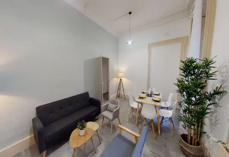 Espace de vie lumineux et bien aménagé avec un canapé sombre, des fauteuils, une table basse et une table à manger dressée; murs neutres et plantes décoratives pour une ambiance conviviale.