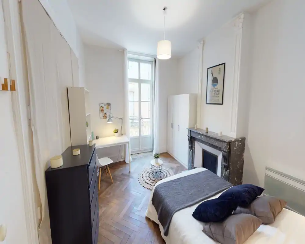Chambre claire et élégante avec un lit double habillé de linge neutre, coussins décoratifs et plaid foncé. La pièce comprend un bureau près d'une grande fenêtre, une cheminée en marbre, une armoire et un parquet point de Hongrie.