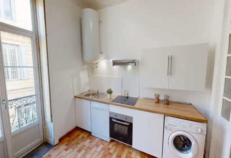 Cuisine compacte et lumineuse avec plan de travail en bois, plaques à induction, four encastré, lave-vaisselle et lave-linge. Grande fenêtre/porte apportant une belle lumière naturelle.