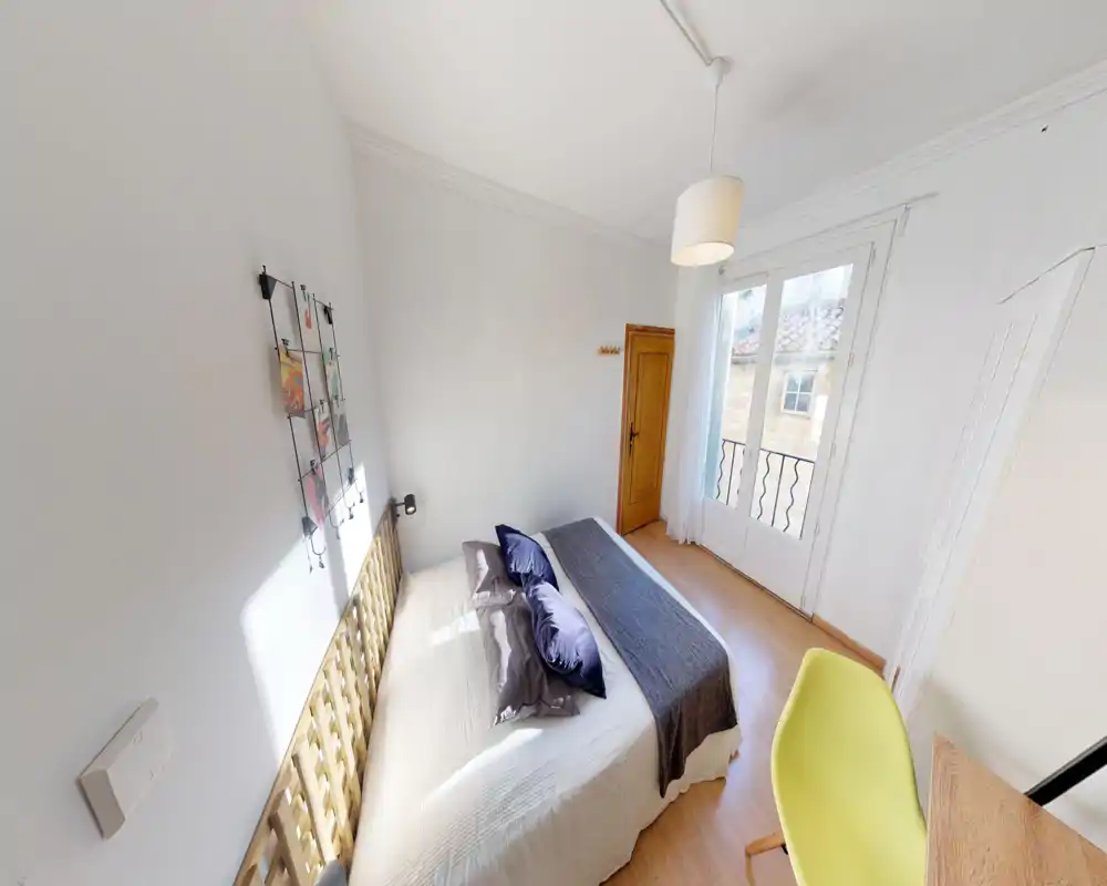 Chambre lumineuse et soignée avec lit double, linge doux et lumière naturelle provenant des portes-fenêtres donnant sur un petit balcon.