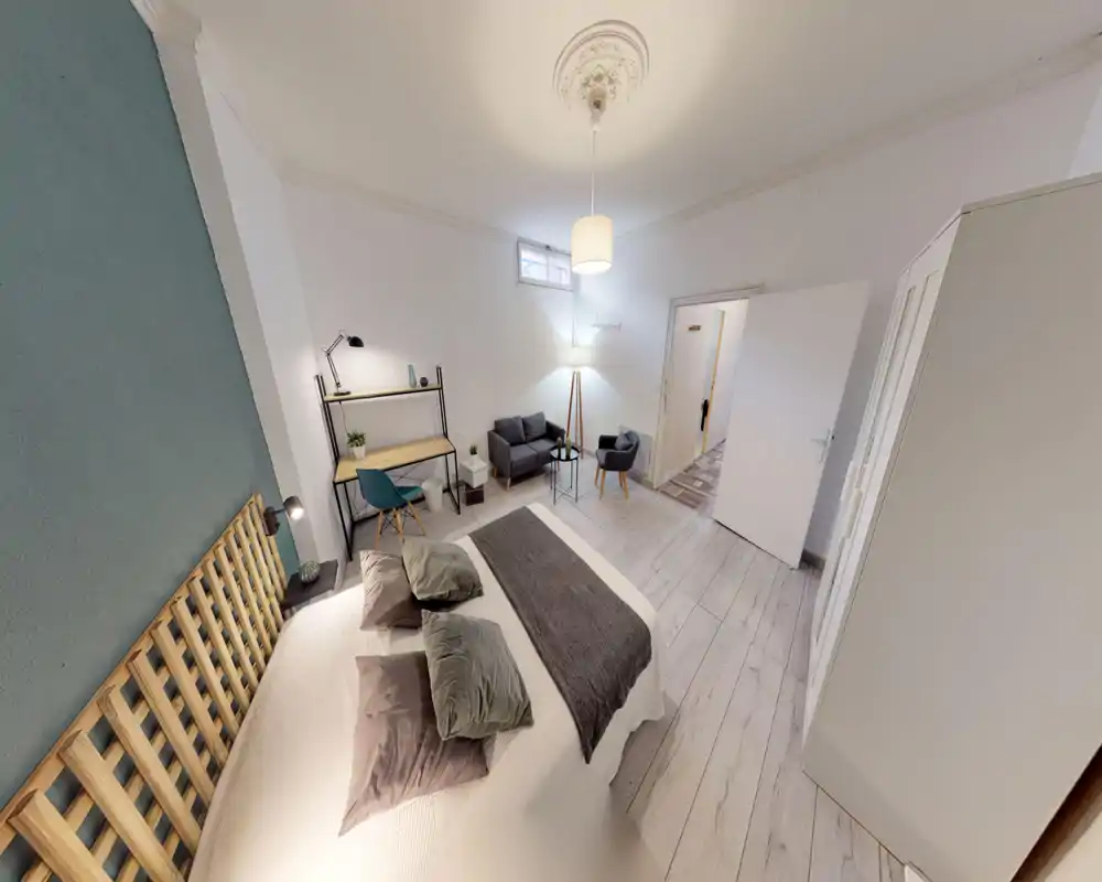 Spacious, well-styled bedroom with a large bed, wooden slatted headboard, desk area and a small seating corner—bright and welcoming for guests.