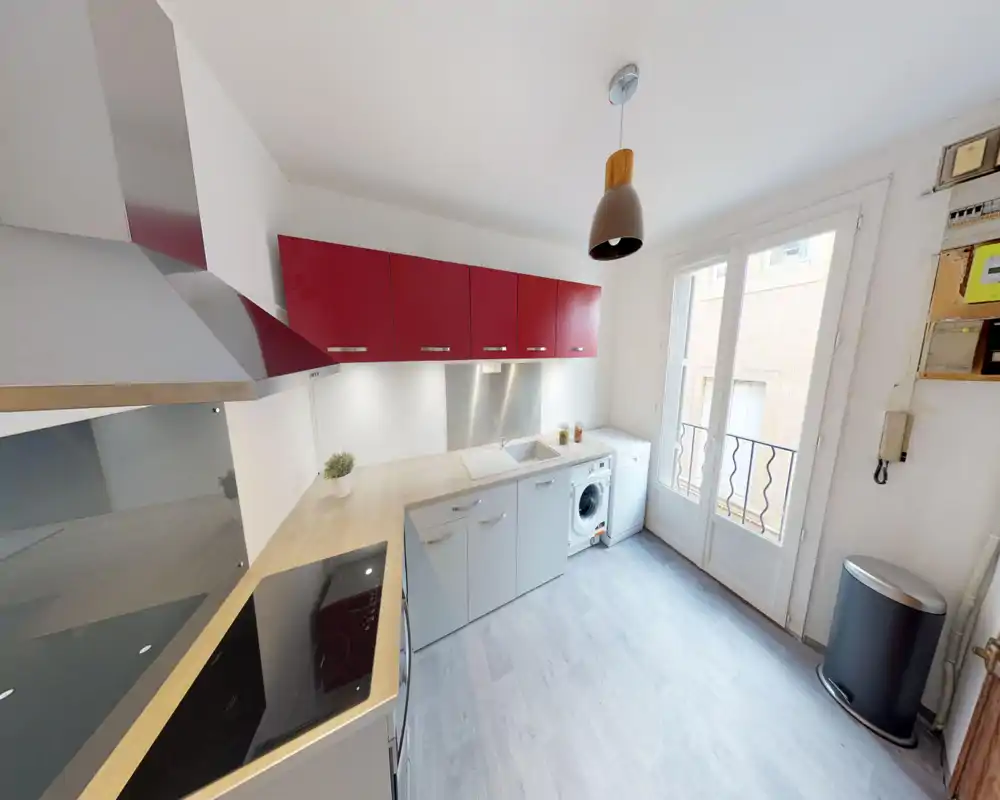 Cuisine moderne et lumineuse avec placards rouges, appareils intégrés, plan de travail en bois et grande fenêtre apportant beaucoup de lumière naturelle.