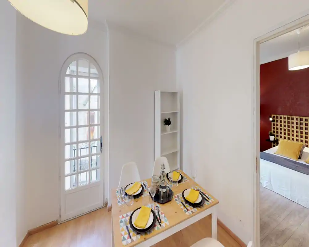 Coin repas lumineux et soigné avec table dressée pour quatre, chaises modernes et lumière naturelle depuis une porte en verre arquée ; étagère ordonnée pour rangement et style.