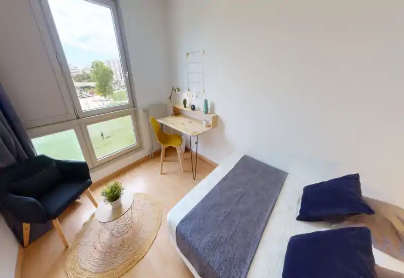 Chambre lumineuse et moderne avec grande fenêtre, textiles chaleureux et un petit bureau — idéale pour une personne ou un étudiant.