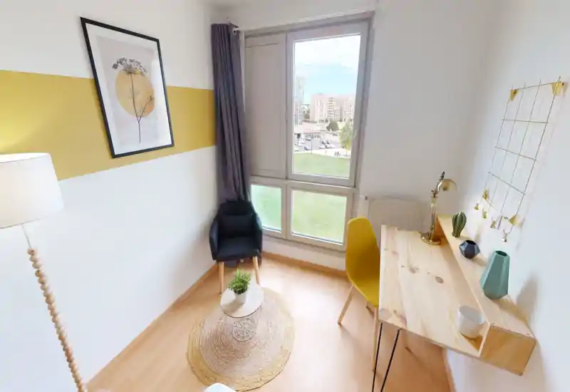 Coin salon lumineux et moderne avec un fauteuil confortable, une petite table basse et un bureau en bois près d'une grande fenêtre — idéal pour se détendre ou travailler à la lumière naturelle.