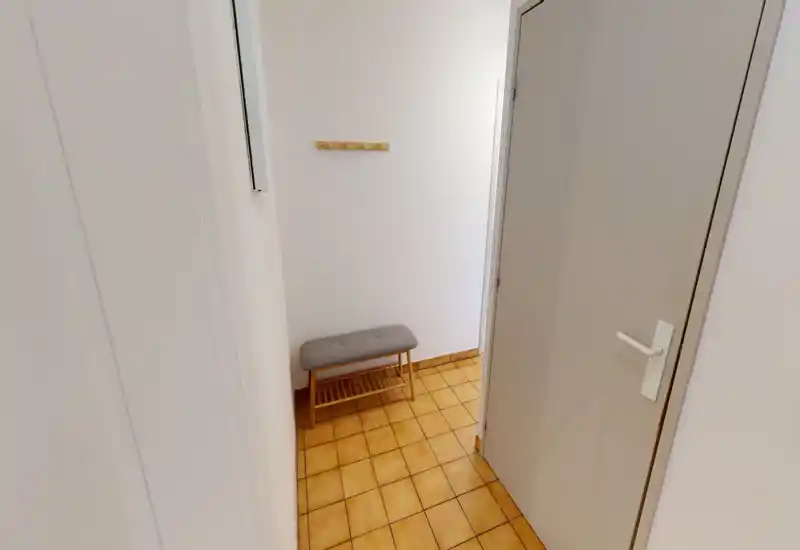 Petit hall d'entrée soigné avec un banc rembourré, des patères murales et un sol carrelé — espace lumineux et fonctionnel pour chaussures et manteaux.