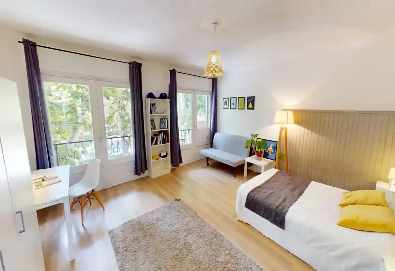 Bright, well-styled bedroom with a single bed, cozy textiles, a small sofa and large windows overlooking trees — ideal for a peaceful stay.