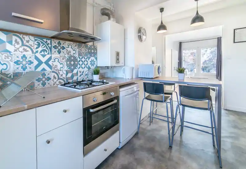 Bright, modern kitchen with patterned tile backsplash, gas hob, built-in oven and a breakfast bar with stools — perfect for casual meals.