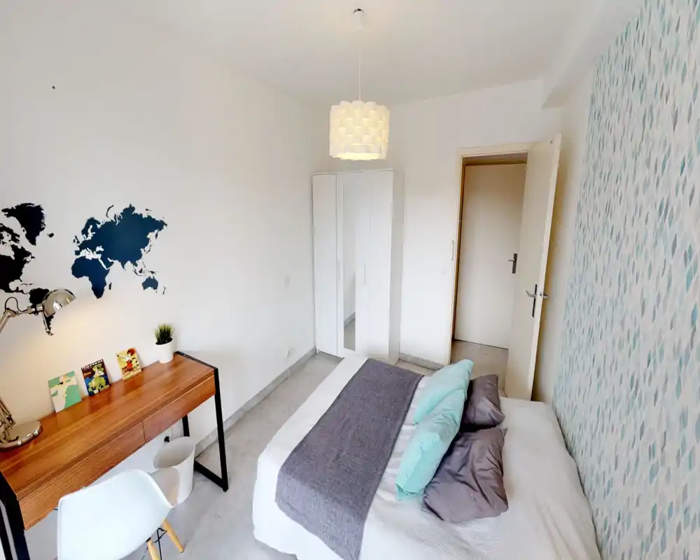 Chambre moderne et lumineuse avec un lit double habillé de linge neutre, coussins décoratifs et un mur d'accent bleu; comprend un bureau en bois et une armoire blanche.