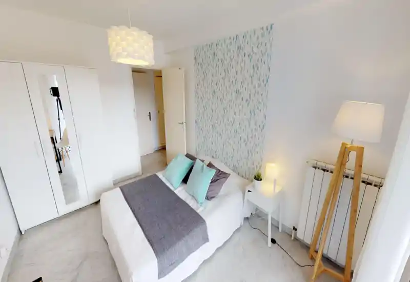 Chambre lumineuse et soignée avec lit double, coussins décoratifs et plaid, armoire à portes miroir et éclairage de chevet chaleureux.