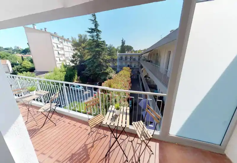 Balcon ensoleillé avec petite table et chaises, donnant sur une cour arborée et des bâtiments voisins — idéal pour un café le matin ou se détendre à l'extérieur.