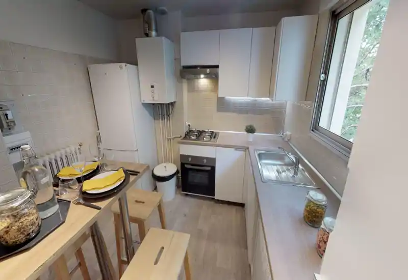 Cuisine compacte et bien équipée avec plaque à gaz, four encastré, évier près de la fenêtre et petit bar pour deux personnes — lumineuse et bien présentée.