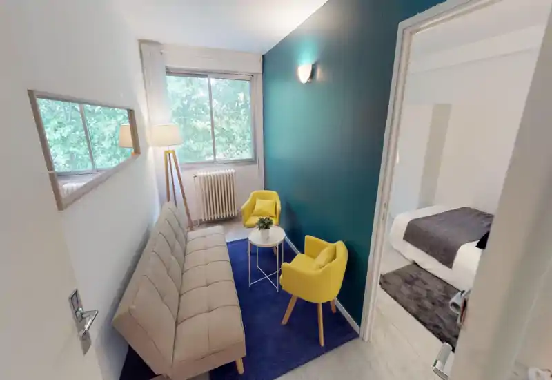 Coin salon compact et élégant avec un canapé beige, deux fauteuils jaunes et un tapis bleu près d'une grande fenêtre qui apporte une belle lumière naturelle.