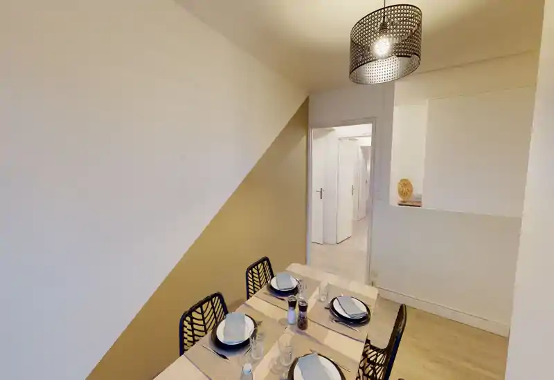 Coin repas moderne et lumineux avec une table dressée pour quatre, un luminaire suspendu décoratif et des chaises contemporaines — idéal pour des repas conviviaux.