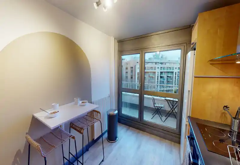 Cuisine moderne et compacte avec un bar pour le petit-déjeuner et des tabourets, grandes portes-fenêtres donnant sur un petit balcon — lumineuse et fonctionnelle pour un appartement urbain.