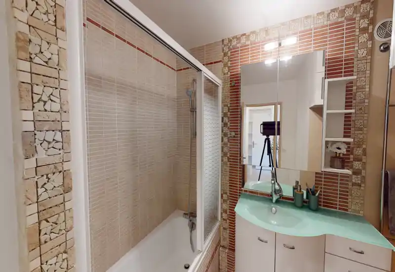 Salle de bain lumineuse et soignée avec baignoire/douche combinée, murs carrelés et lavabo moderne avec meuble et miroir.