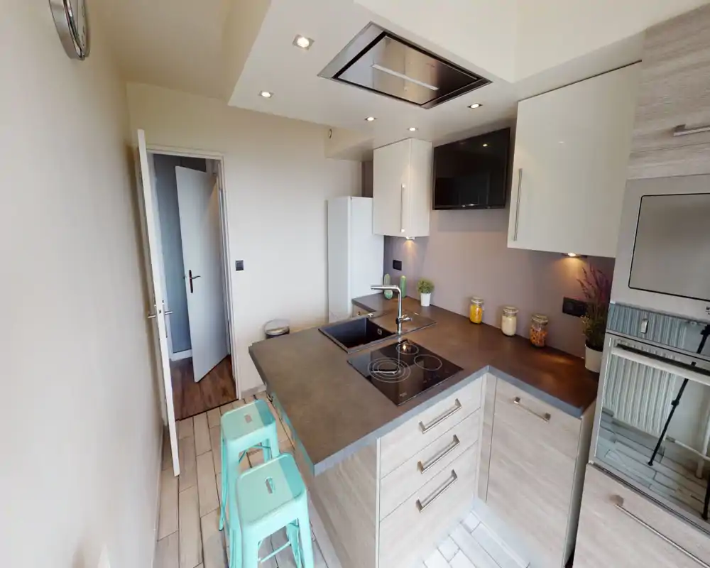 Modern compact kitchen with an island countertop, induction hob, built-in oven and integrated sink; light wood cabinets and small decorative jars create a warm, functional space ideal for a small apartment.
