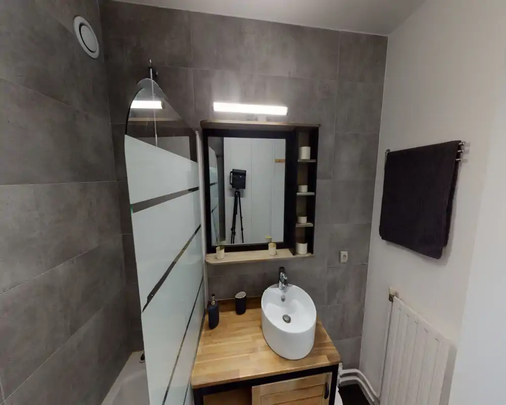 Compact modern bathroom with a vessel sink on a wooden vanity, tiled walls and a frosted glass shower screen; well-lit and neatly arranged.