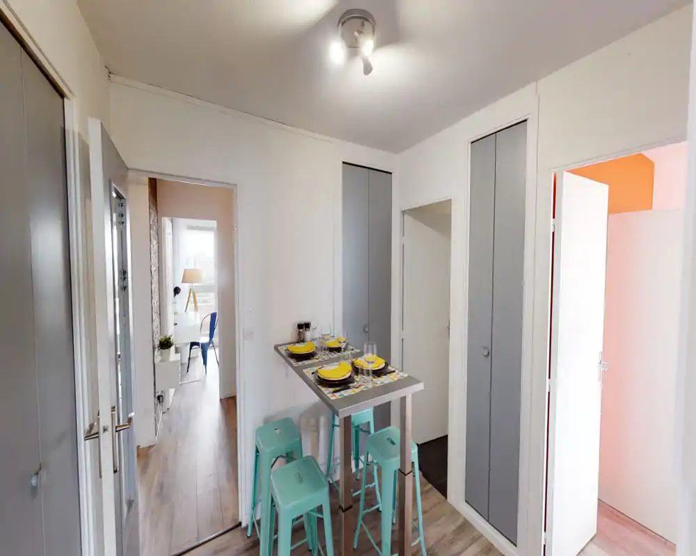 Bright, modern living area with a high breakfast table set for four and mint-green stools; clean white walls, wooden floors and built-in storage create a tidy, functional space.