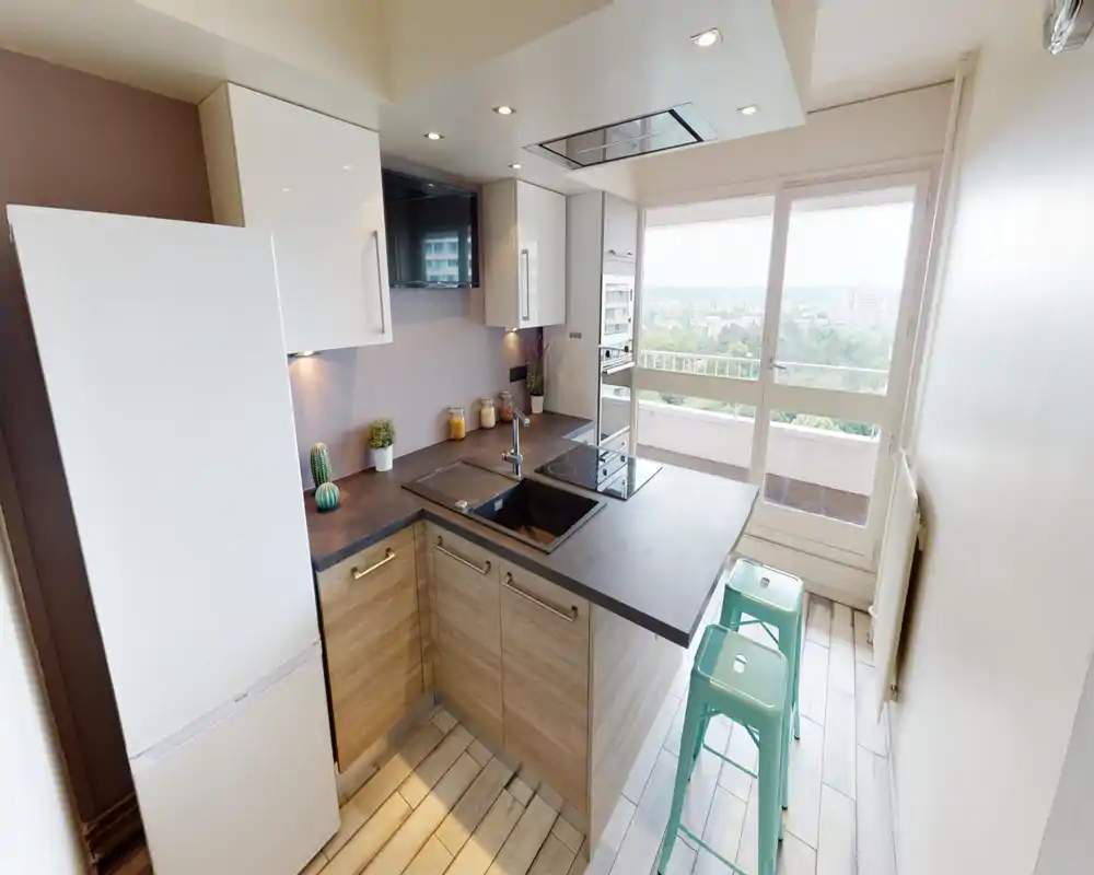 Bright modern kitchen with an L-shaped countertop, integrated sink and hob, white cabinets and large windows offering a city view.