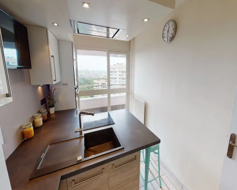 Modern compact kitchen with a dark countertop island, built-in sink and induction hob, bright window with balcony view and stylish storage jars—ideal for a city apartment.