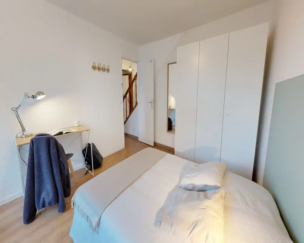 Chambre lumineuse et moderne avec lit double, linge de lit doux, armoire et petit bureau avec lampe — idéale pour une personne ou un couple.